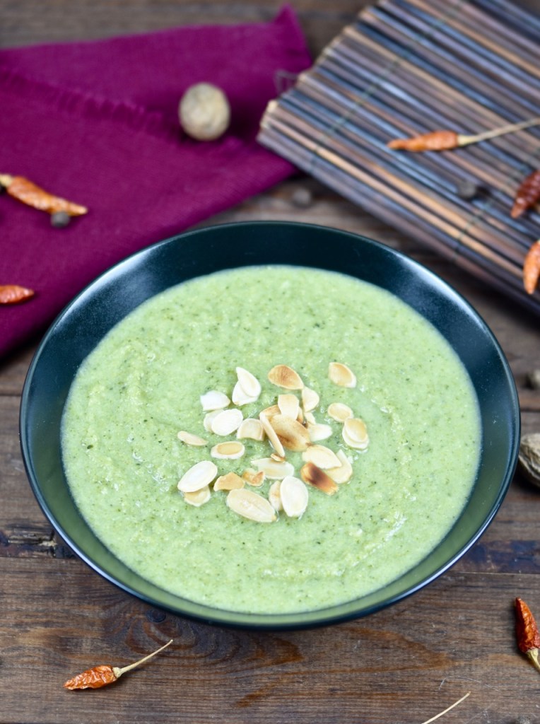 cremige Brokkolisuppe in schwarzer Schale, dekoriert mit Mandelplättchen. Hintergrund dunkel