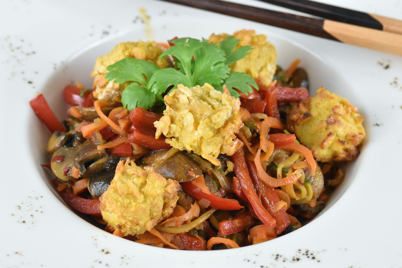 Asiatisches Wokgemüse mit knusprigem Tofu auf weißem Teller. Hintergrund dunkel.