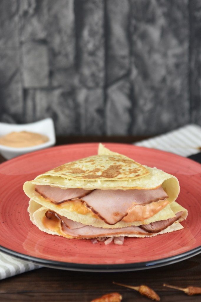 Reuben Sandwich-Tortilla Wrap auf rotem Teller. Hintergrund dunkel.