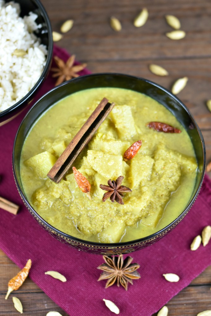 Veganes Kartoffelcurry in einer schwarzen Schale. Im Hintergrund steht der Kokosreis in einer anderen asiatischen Schale.