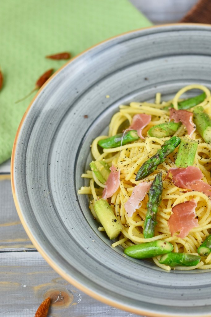 Orangen-Nudeln mit grünem Spargel in einem grauen tiefen Teller. Hintergrund hell.