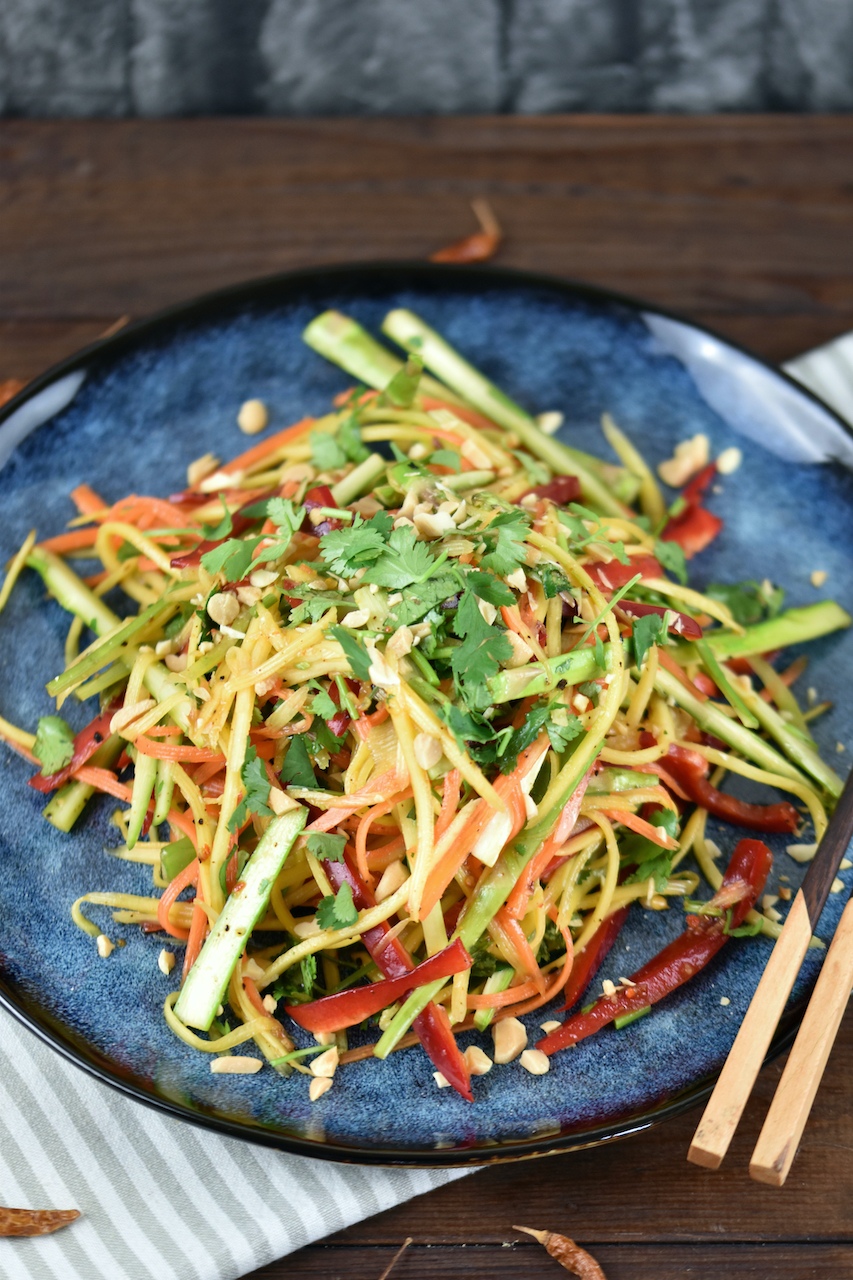Thai Salat mit Mango und gerösteten Erdnüssen auf einem blauen Teller.