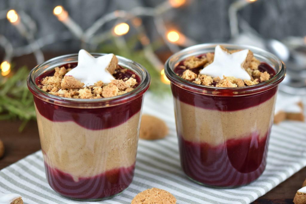 Zimtcreme mit Kirschsauce und Amarettini-Crunch in 2 Gläsern. Hintergrund dunkel.