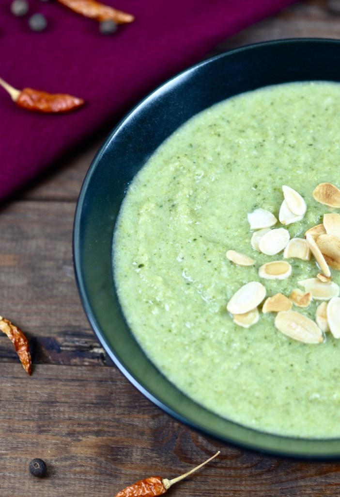 cremige Brokkolisuppe in schwarzer Schale, dekoriert mit Mandelplättchen. Die Schale ist nur halb zu sehen. Hintergrund dunkel