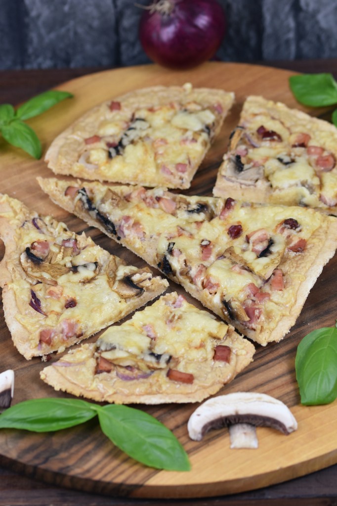 Veganer Flammkuchen mit Champignons und Basilikum auf Holzbrett.