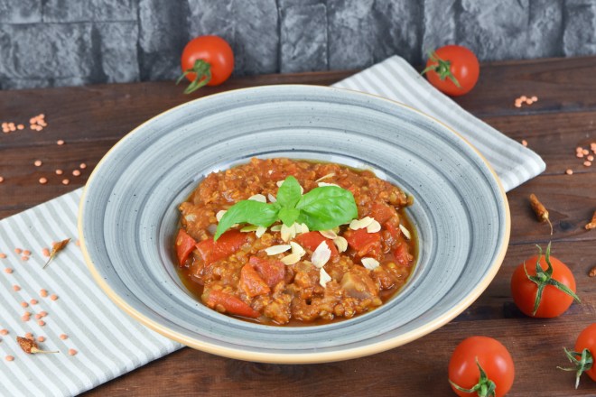 Italienischer Eintopf mit Tomaten, Paprika und Linsen in grauem Teller. Hintergrund dunkel.