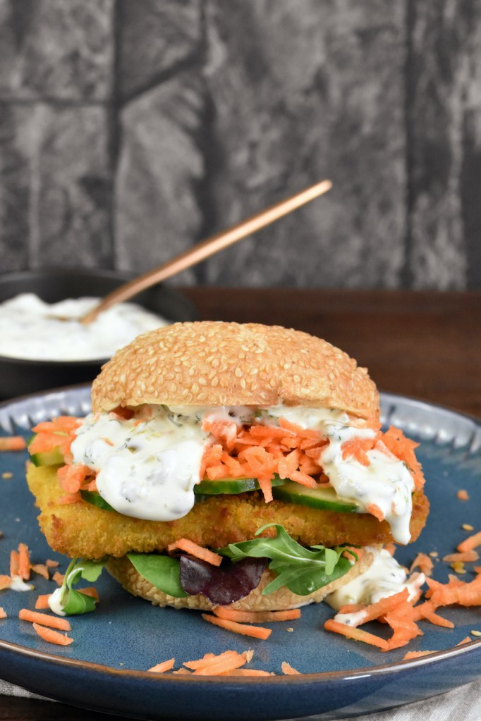 Veganer Fischburger mit Jalapeño-Remoulade auf blauem Teller.