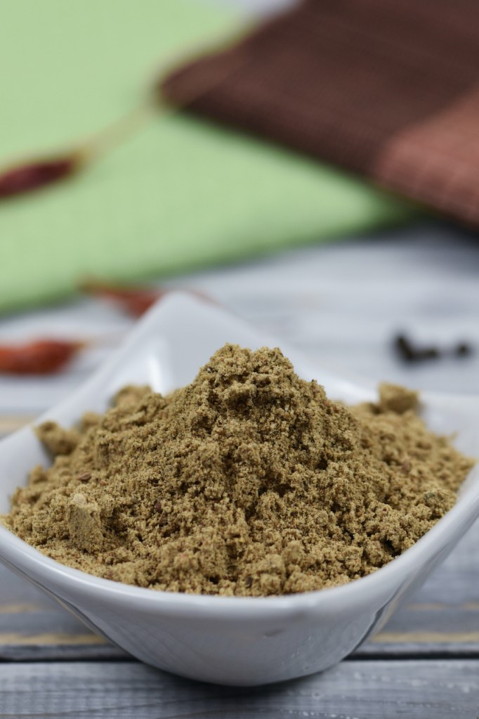 Chat Masala in weißer Schale. Heller Hintergrund, dekoriert mit Gewürzen.