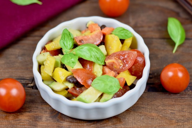 Bunter Avocado-Salat mit Tomaten in weißer Schale. Dekoriert mit Basilikum. Hintergrund dunkel
