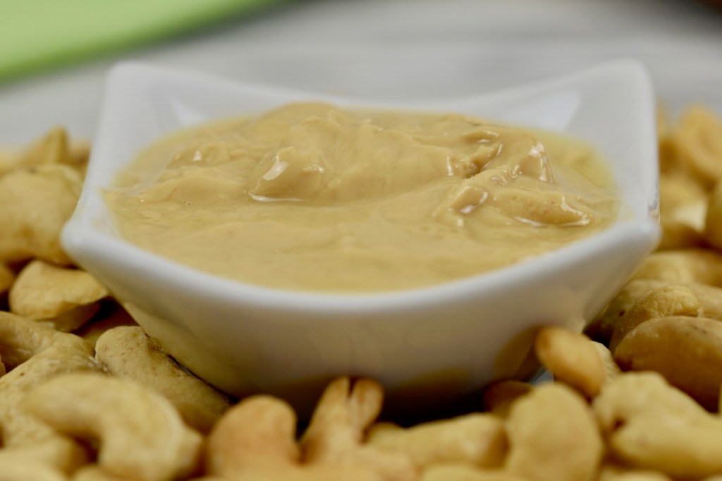 Cashewmus in einem weißen Porzelanschälchen. Drumherum liegen Cashewkerne. Nahaufnahme