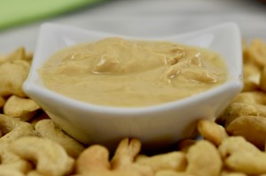 Cashewmus in einem weißen Porzelanschälchen. Drumherum liegen Cashewkerne. Nahaufnahme