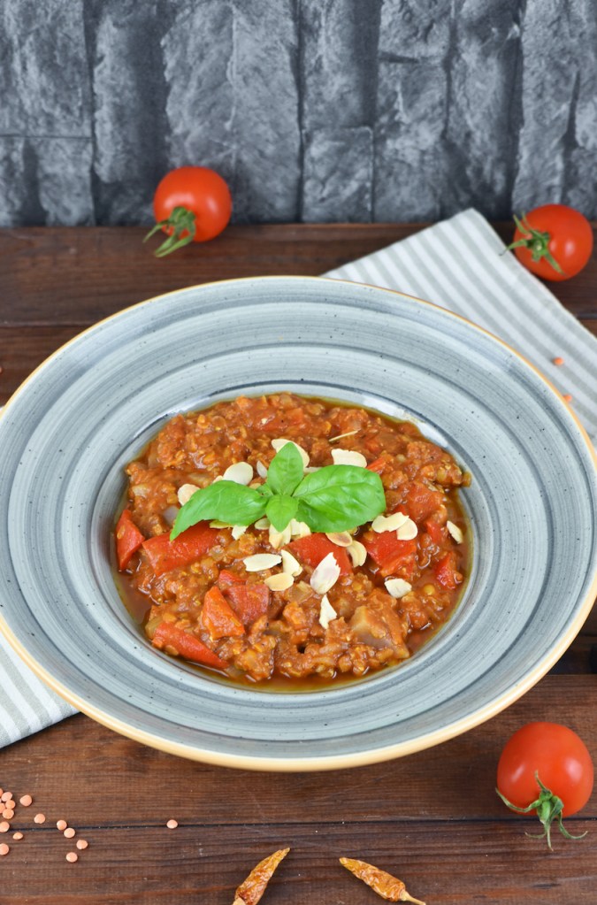 Italienischer Eintopf mit Tomaten, Paprika und Linsen in grauem Teller. Hintergrund dunkel.