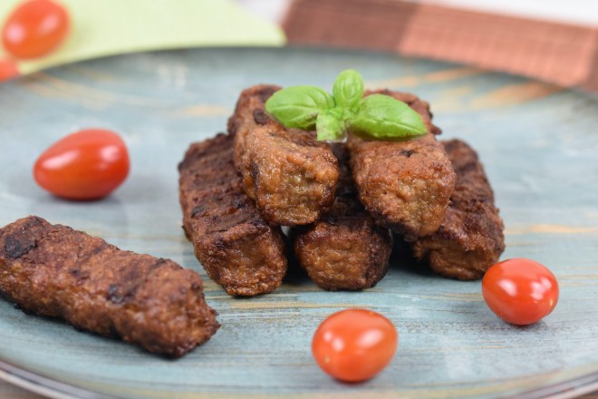 Mehrere Mici oder Mititei auf einem bläulichen Teller. Hintergrund hell.