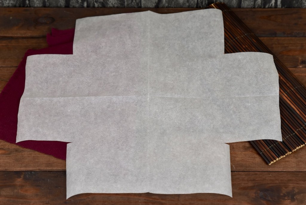 Das eingeschnittene Backpapier ist aufgefaltet. Es sieht aus wie ein dickes Kreuz. Hintergrund dunkel.