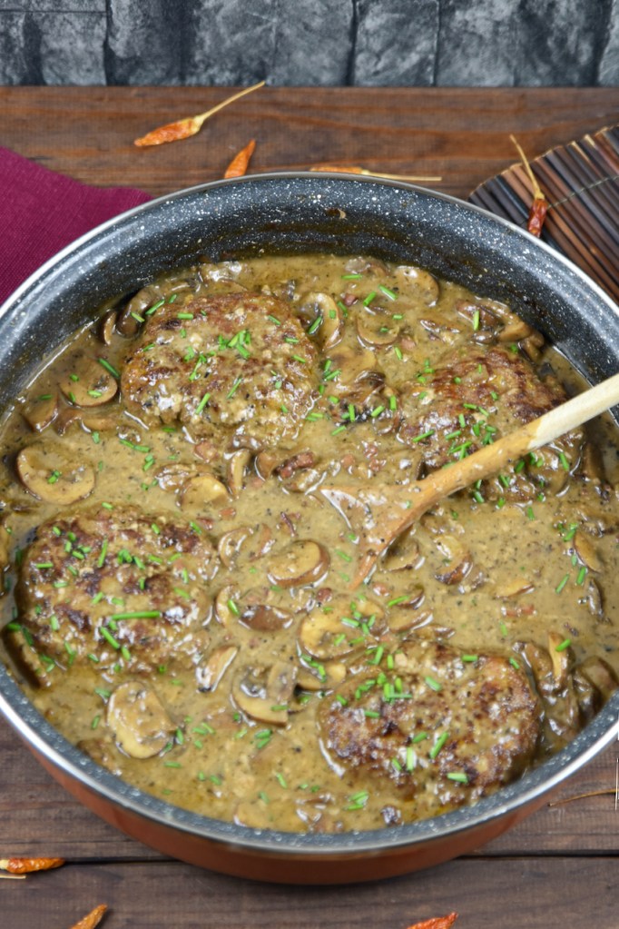 Frikadellen aus dem Backofen in cremiger Pilzsauce in einer tiefen Pfanne. Hintergrund dunkel.