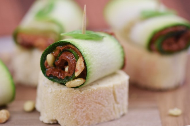 Zucchini-Röllchen mit Paprikacreme und Pinienkernen gefüllt auf Holzbrett.