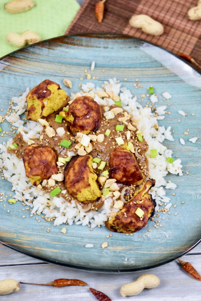 Knusprige Blumenkohlröschen mit Erdnusssauce und Reis, garniert mit Erdnüssen und Frühlingszwiebeln.