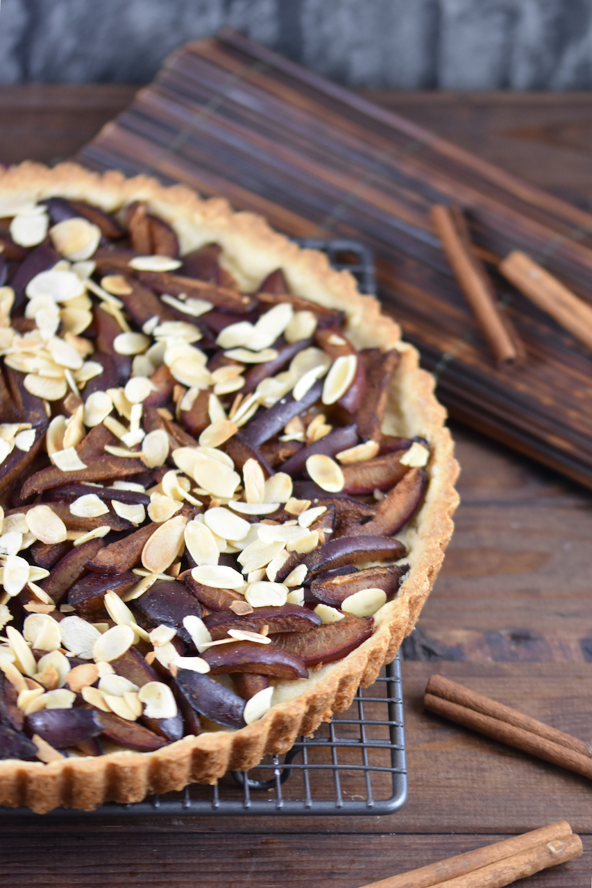 Glutenfreie Pflaumen-Tarte mit Zimtstreuseln. Hintergrund dunkel.