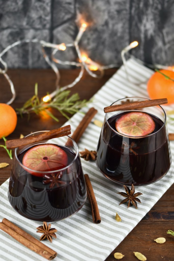 Klassischer Glühwein in 2 Gläsern auf hellem Tuch. Hintergrund dunkel.