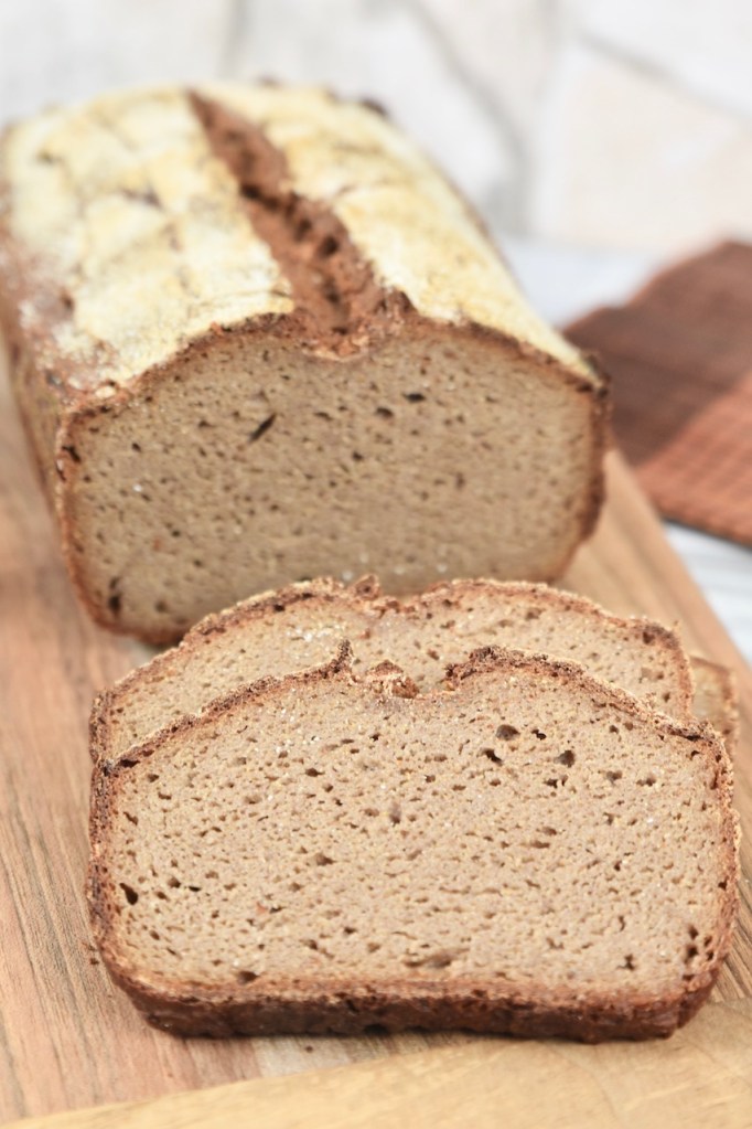 glutenfreies Krustenbrot in Kastenform auf Holzbrett mit 2 angeschnittenen Scheiben. Hintergrund hell.