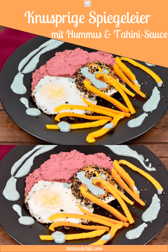 Knusprige Spiegeleier mit einer Kruste aus Sesam und Schwarzkümmelsamen mit pinkem Rote Beete Hummus und grüner Tahini-Sauce. Dazu gibt es gelbe Paprikastreifen Angerichtet ist alles auf einem schwarzen Teller.