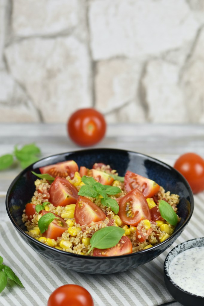 Quinoa Salat mit Avocado in einer schwarzen Schale. Daneben steht in einer kleineren Schale der Minz-Joghurt.