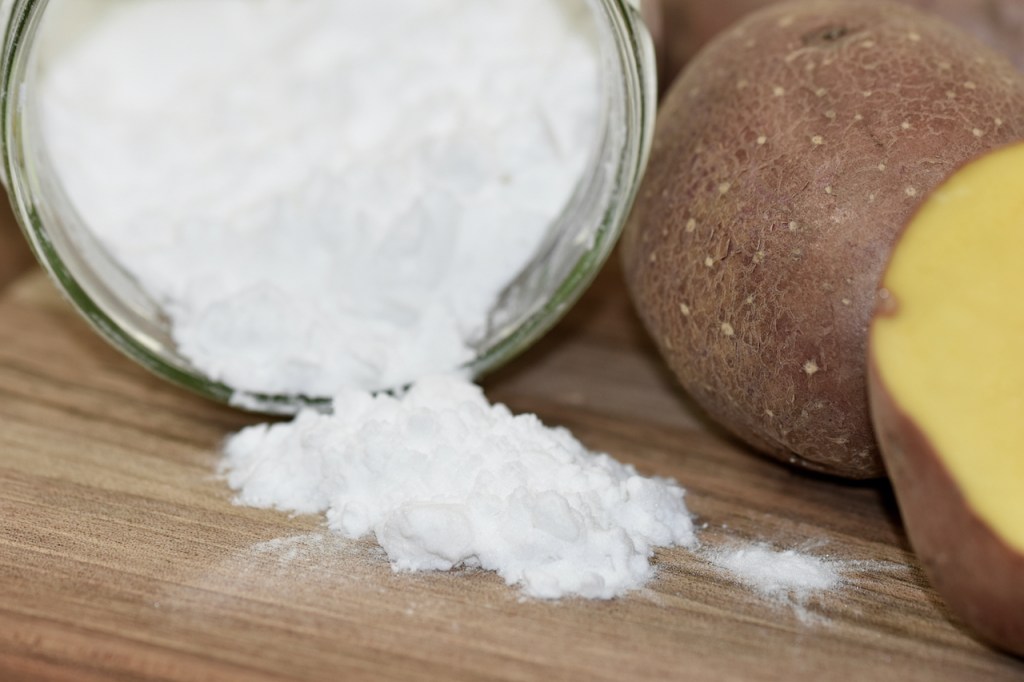 Kartoffelstärke im Glas, daneben liegen Kartoffeln.