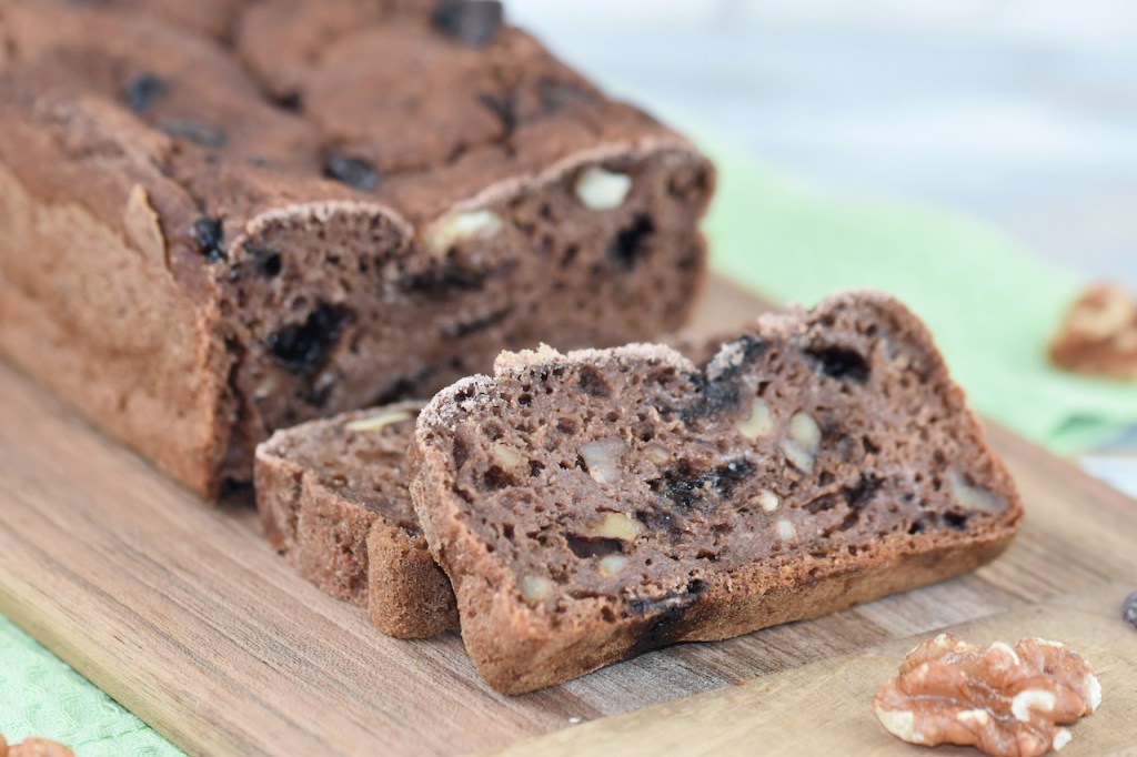 Angeschnittenes Bananenbrot mit Schokolade und Walnüssen auf Holzbrett. Hintergrund hell.