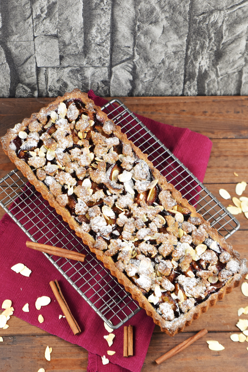 Glutenfreie Pflaumen-Tarte mit Zimtstreuseln. Hintergrund dunkel.