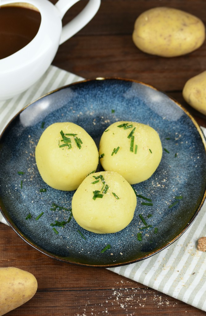 Drei Kartoffelklöße liegen auf einem auf dunkelblauem Teller.