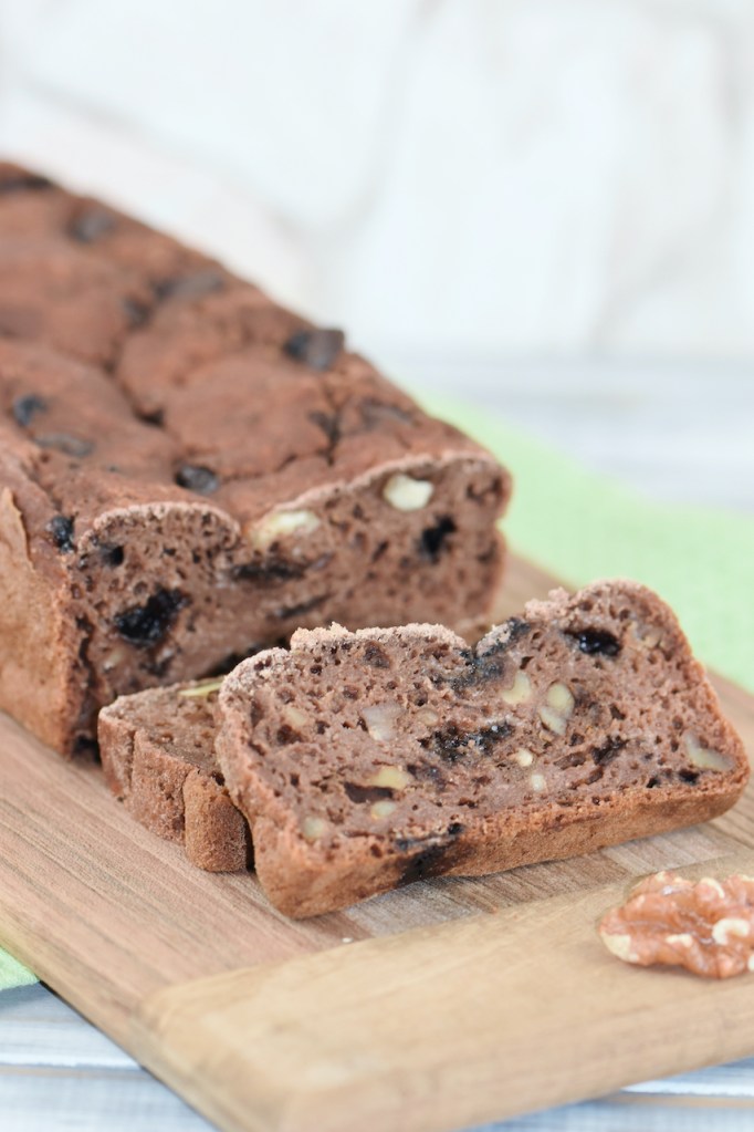 Angeschnittenes Bananenbrot mit Schokolade und Walnüssen auf Holzbrett. Hintergrund hell.