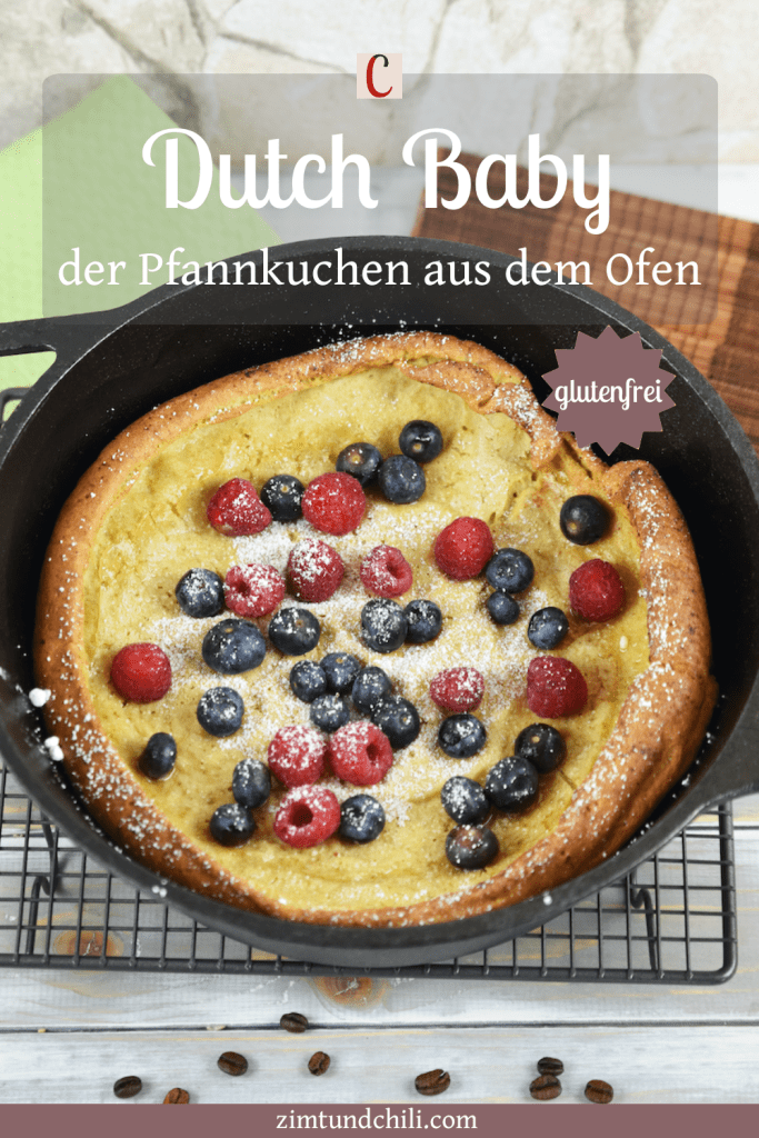 Glutenfreier Dutch Baby im schwarzen Gusseisentopf, dekoriert mit Himbeeren, Blaubeeren und Puderzucker. Hintergrund hell.