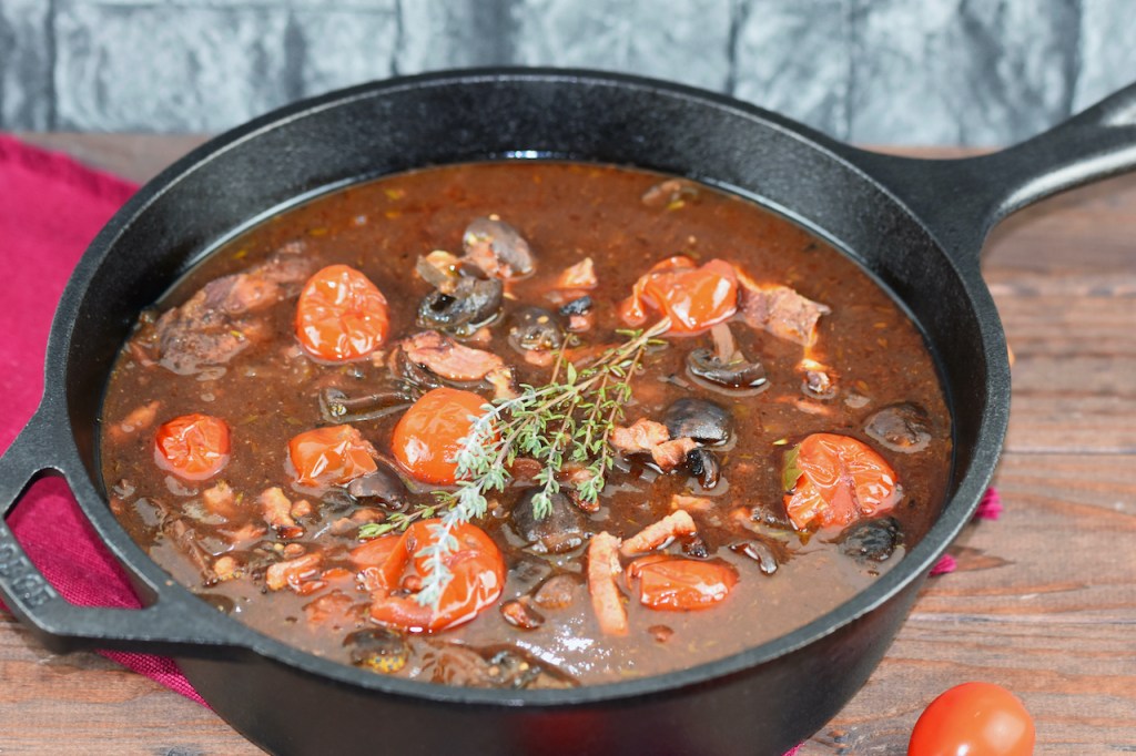 Coq au Vin aus dem Ofen in einem schwarzen Topf aus Gusseisen. Hintergrund dunkel.