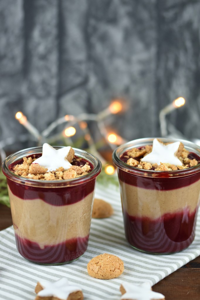 Zimtcreme mit Kirschsauce und Amarettini-Crunch in 2 Gläsern. Hintergrund dunkel.