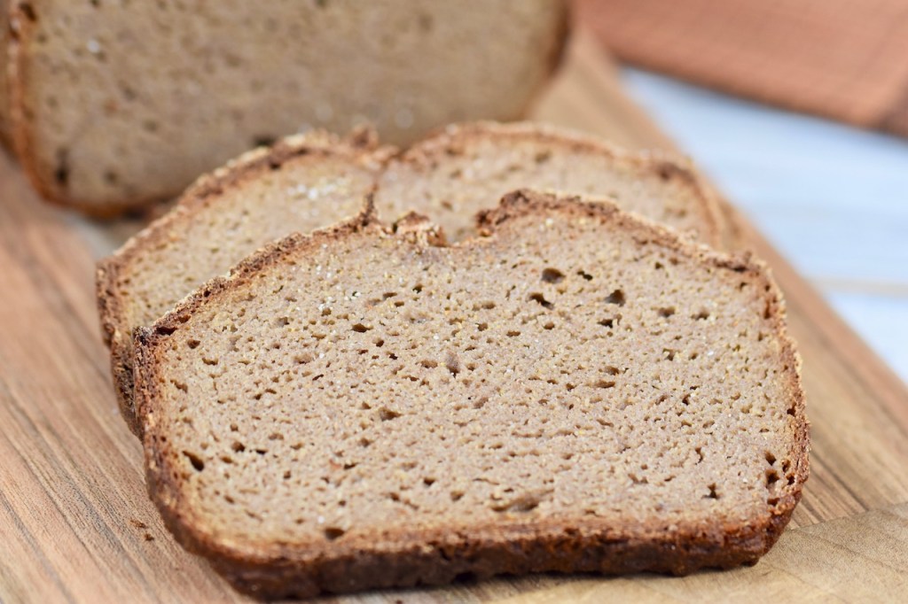 glutenfreies Krustenbrot in Kastenform auf Holzbrett mit 2 angeschnittenen Scheiben. Hintergrund hell.