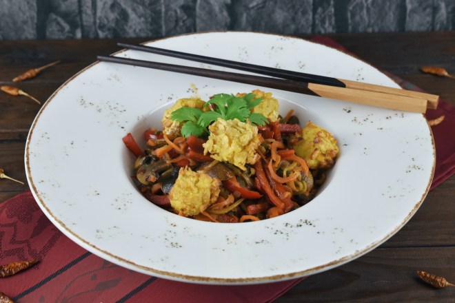 Asiatisches Wokgemüse mit knusprigem Tofu auf weißem Teller. Hintergrund dunkel.