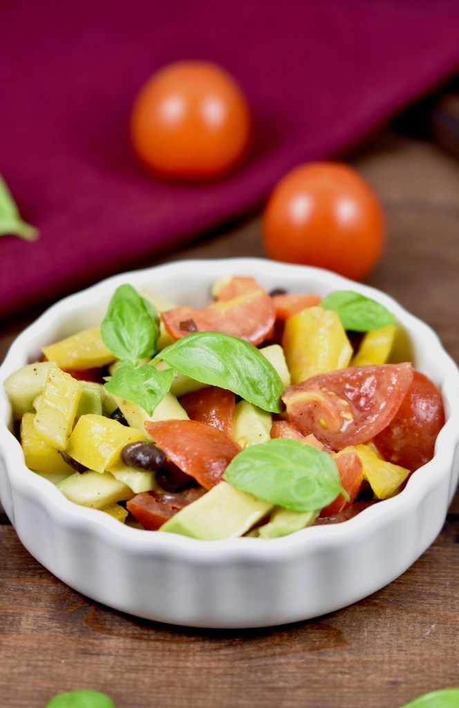 Bunter Avocado-Salat mit Tomaten in weißer Schale. Dekoriert mit Basilikum. Hintergrund dunkel