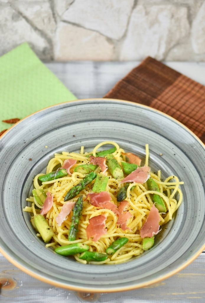 Orangen-Nudeln mit grünem Spargel in einem grauen tiefen Teller. Hintergrund hell.