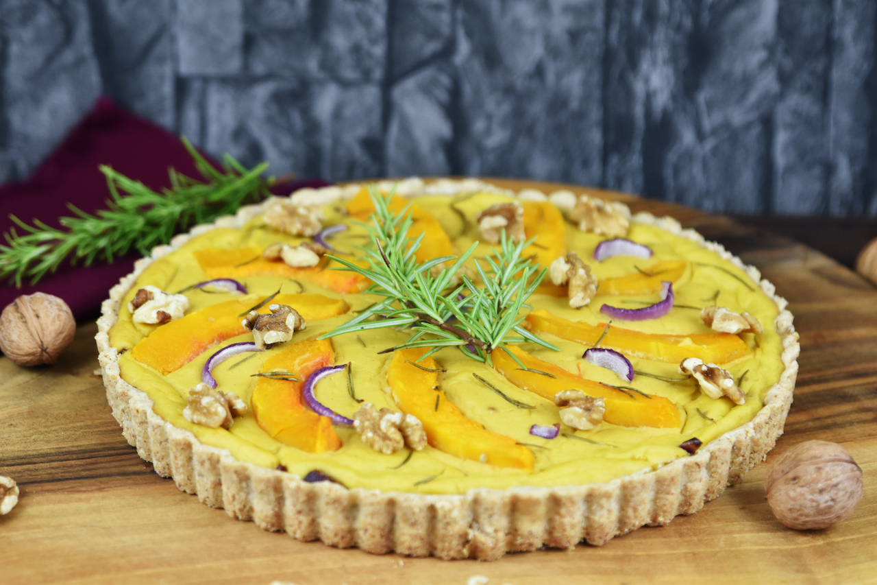 Runde Kürbis-Quiche mit Walnüssen und Rosmarin. Hintergrund dunkel.