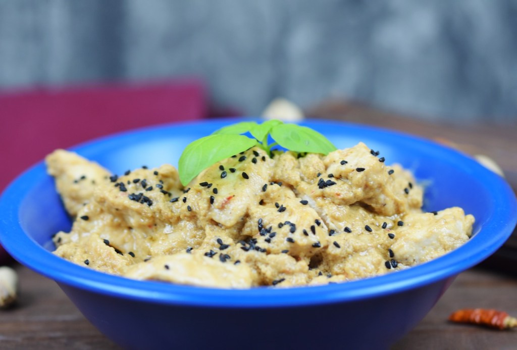 Hähnchen-Mezze in Tahini-Kokossauce in einer blauen Schale garniert mit Basilikum. Hintergrund dunkel.