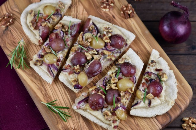 Flammkuchen mit Weintrauben und Walnüssen in Stücke geschnitten auf einem Holzbrett.