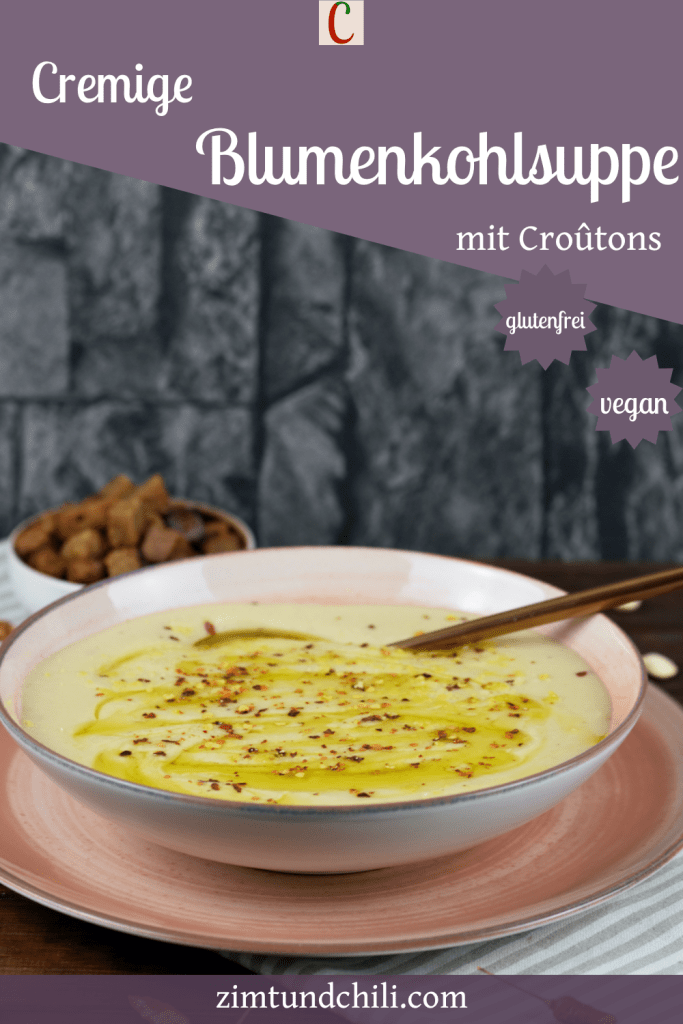 Cremige Blumenkohlsuppe in einem rosa Teller. Im Hintergrund stehen die Croûtons. Beschrifteter Pin.