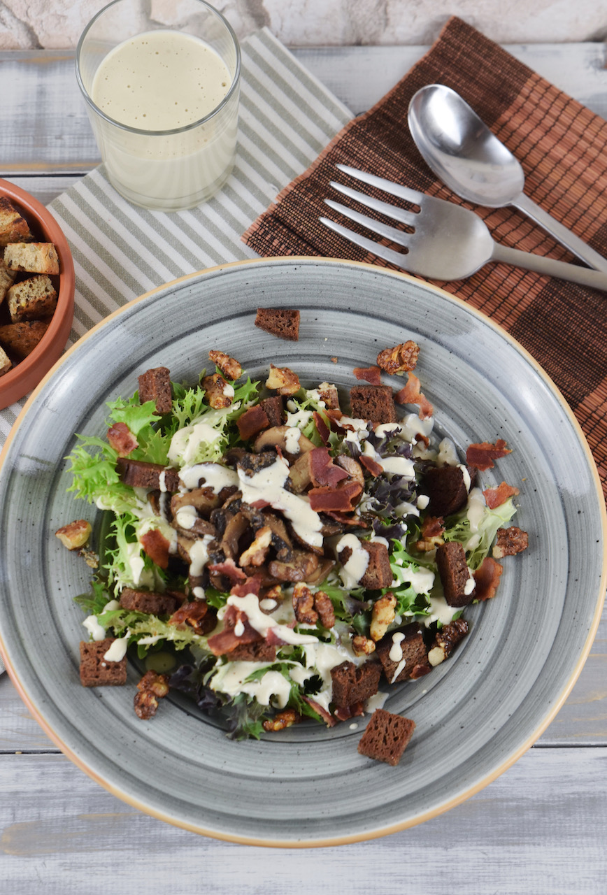 Veganer Caesar Salad mit Pilzen und Walnüssen auf grauem Teller. Hintergrund hell.