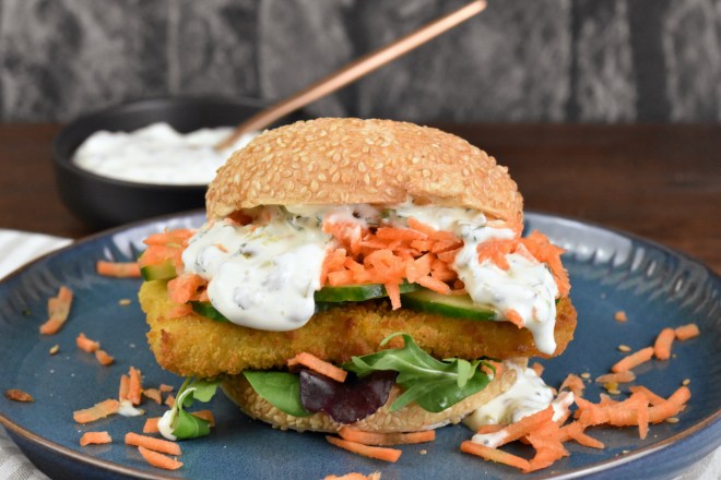 Veganer Fischburger mit Jalapeño-Remoulade auf blauem Teller.