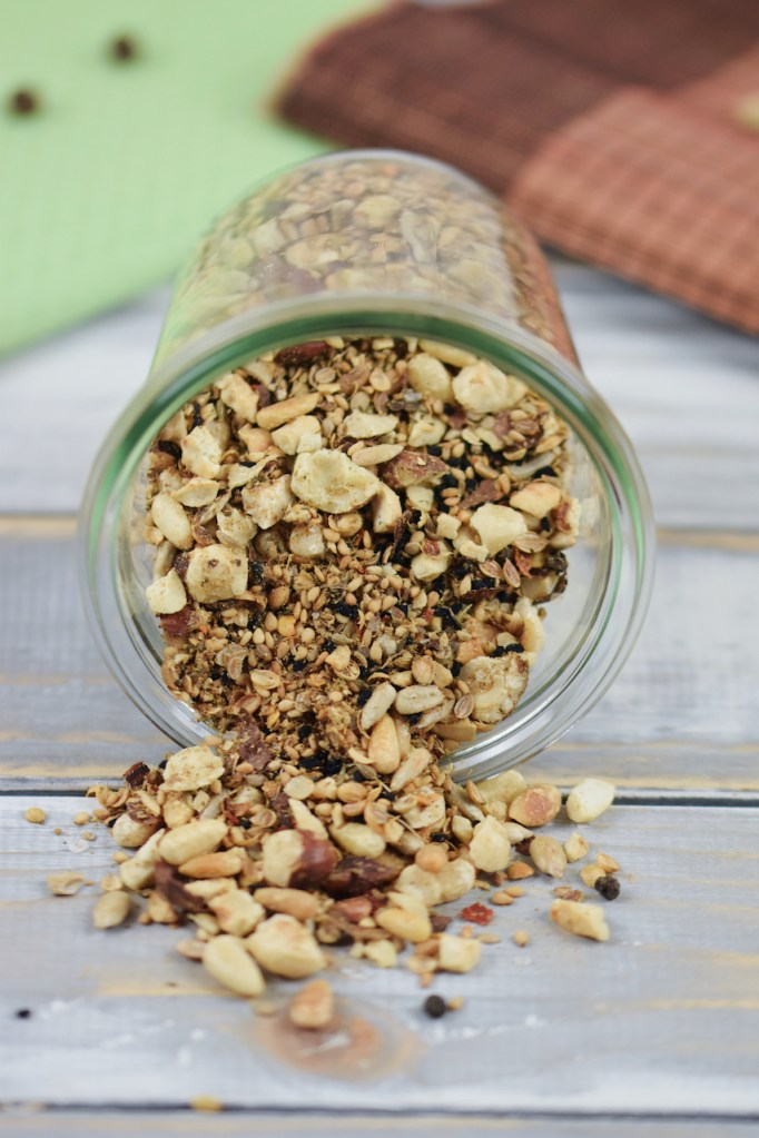 Dukkah selber gemacht in einem liegenden Glas. Etwas Dukkah ist herausgerutscht. Hintergrund hell.