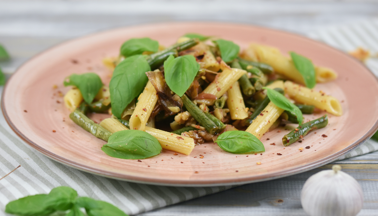 Zitronenpasta mit grünen Bohnen und Walnüssen auf einem rosa Teller.