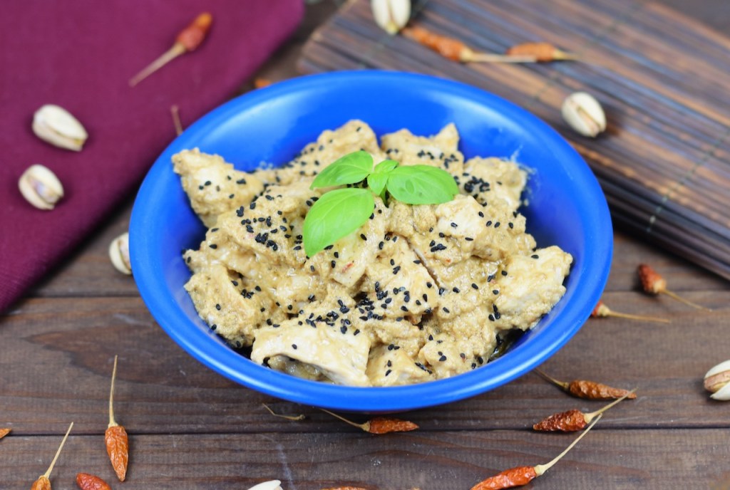Hähnchen-Mezze in Tahini-Kokossauce in einer blauen Schale garniert mit Basilikum. Hintergrund dunkel.