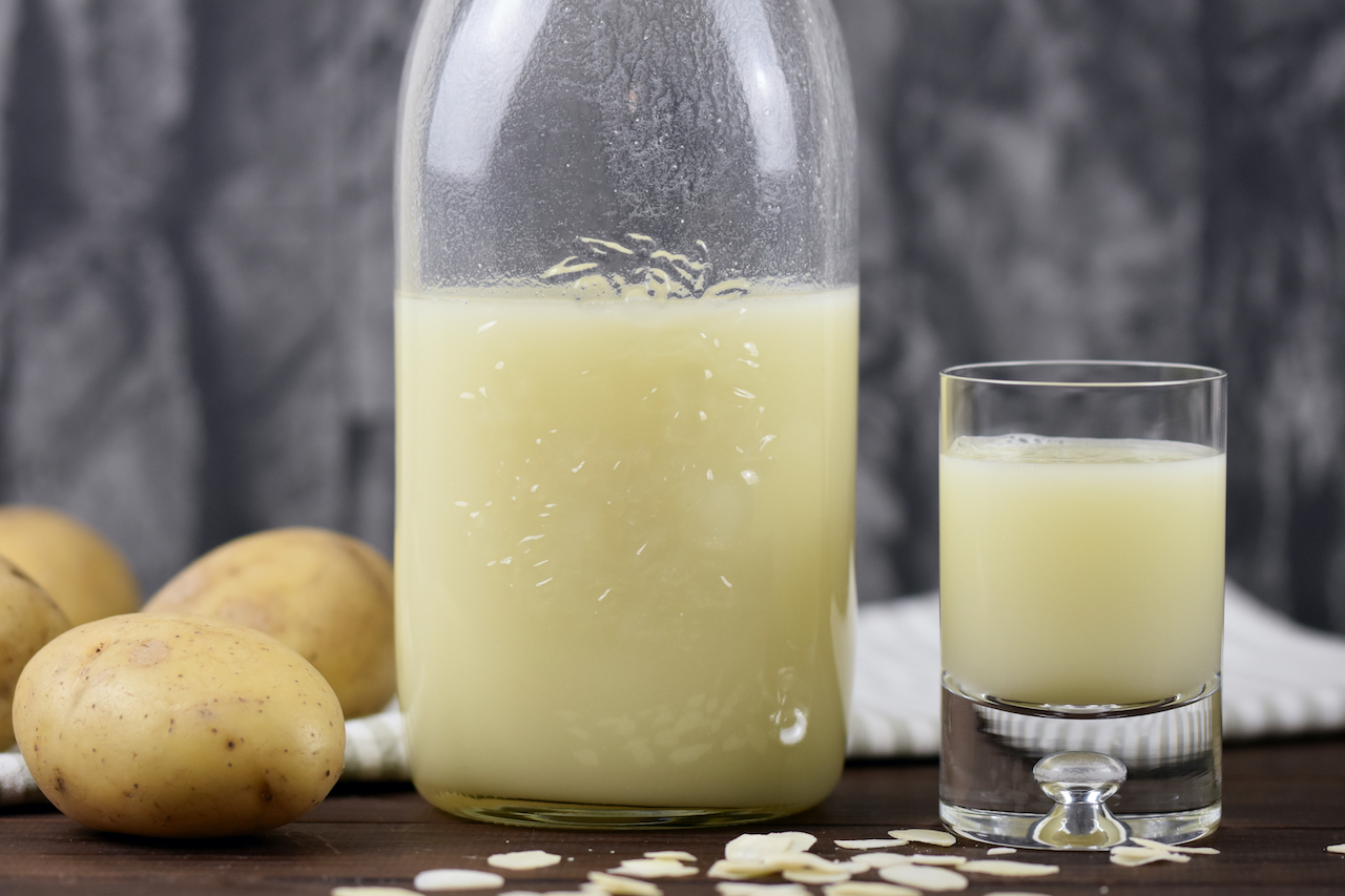 Vegane Milch aus Kartoffeln in einer Glasflasche und einem Glas. Hintergrund dunkel.