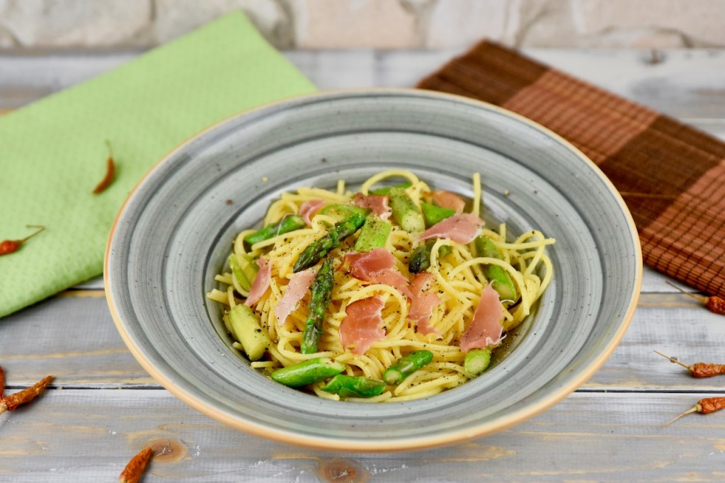 Orangen-Nudeln mit grünem Spargel in einem grauen tiefen Teller. Hintergrund hell.
