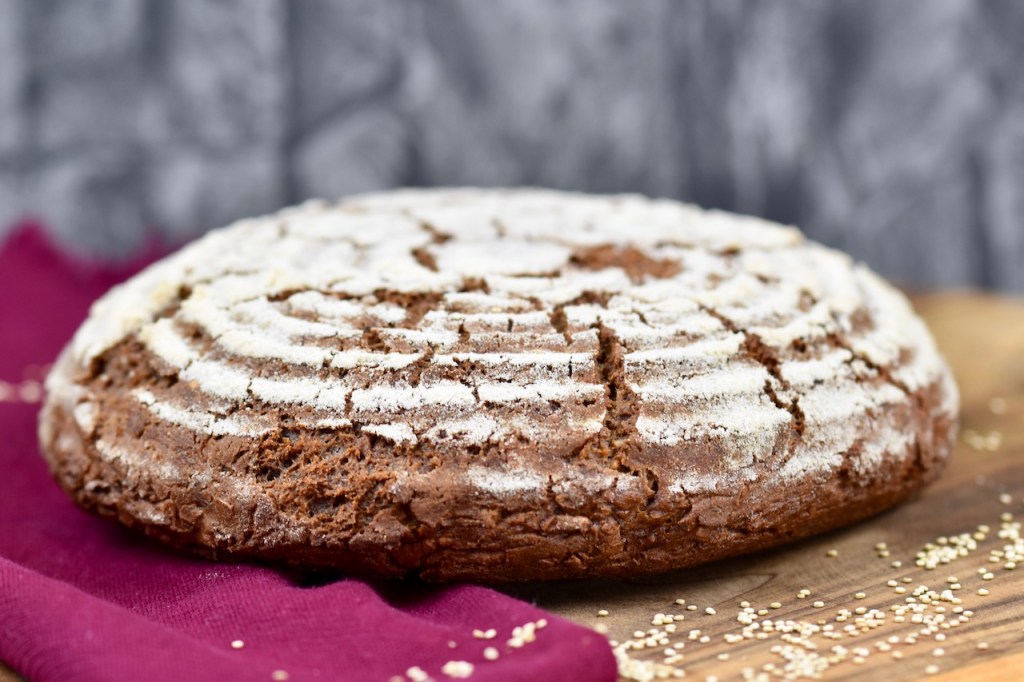 glutenfreies Krustenbrot in rund auf Holzbrett. Dekoriert ist es mit einer weinroten Stoffserviette und groben Salzkörnern.